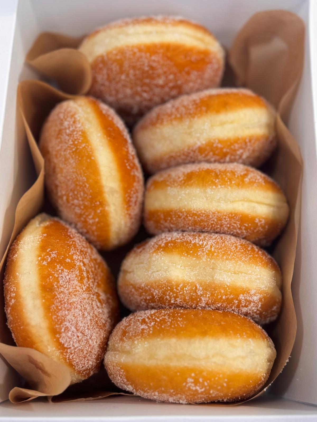 Sugar-coated filled donuts lined up in a white box