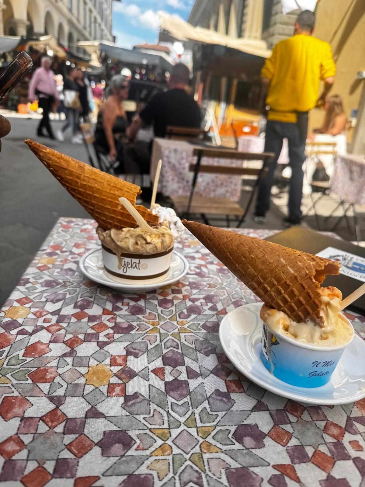 Two gelato cups with waffle cones on a tiled table at a Florence cafe