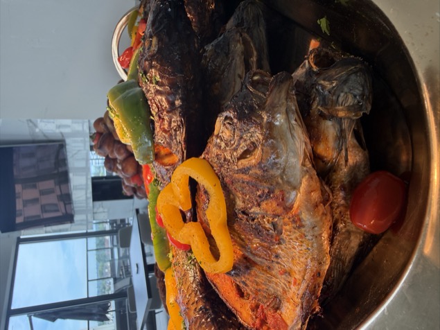 Whole grilled fish stacked on a platter with peppers