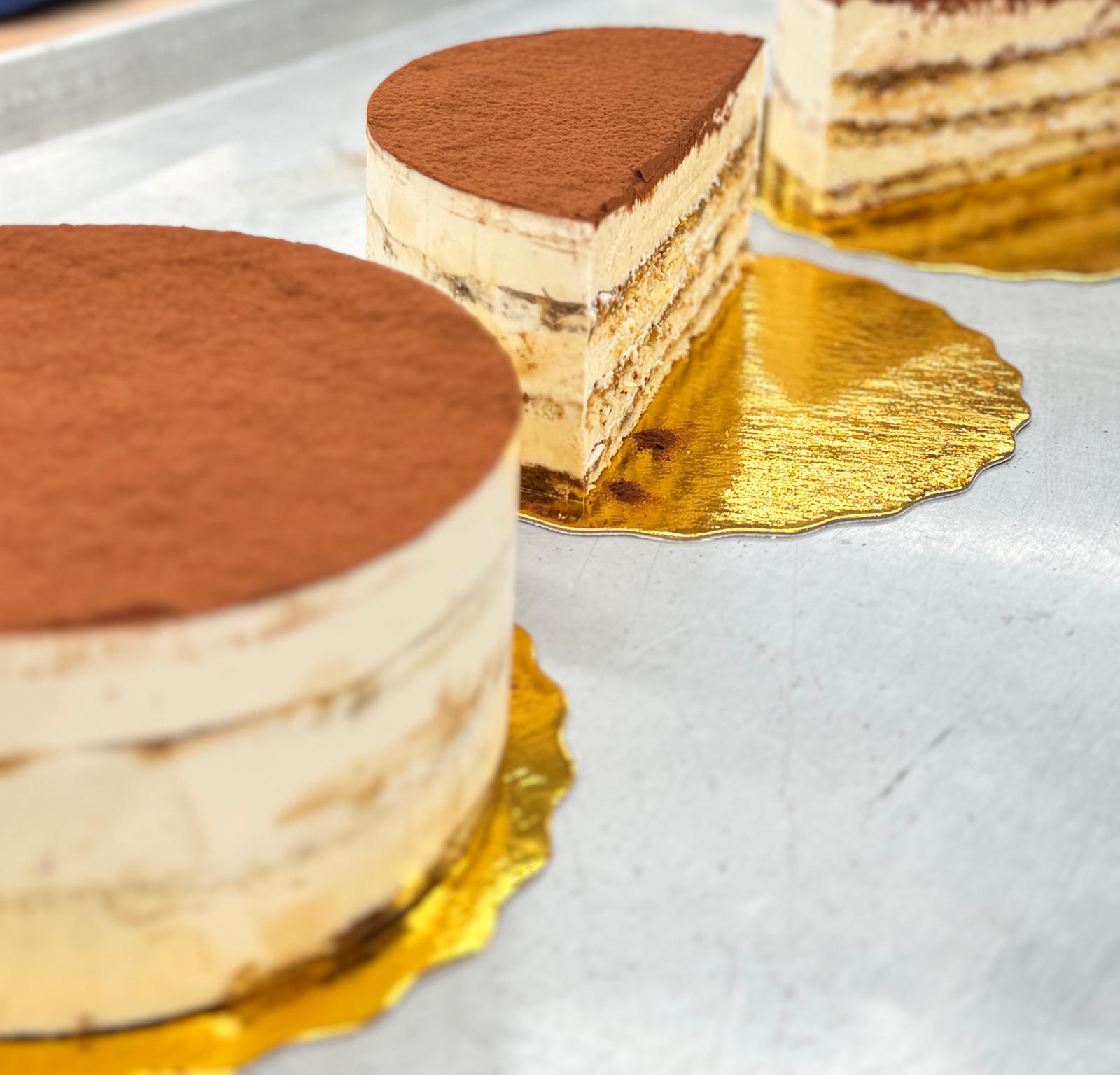 Whole and sliced tiramisu rounds on gold cake boards